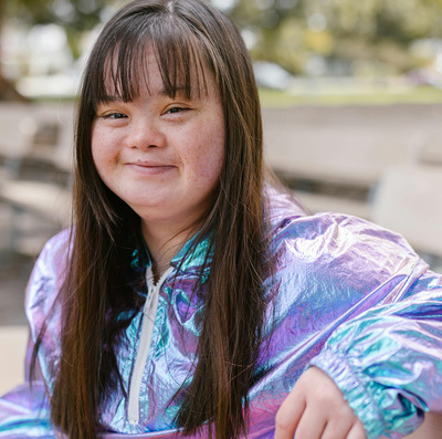 Young woman with Down syndrome sits and smiles in a park.