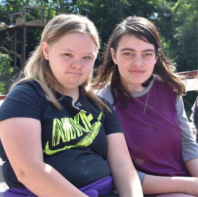 Two friends--a blonde and a brunette woman--sit side by side smiling in the sunshine during an outing to the Lockport Locks.