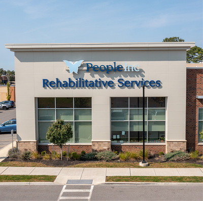 The modern, beige facade of a building with two nine-pane windows and signage that reads "People Inc. Rehabilitative Services."