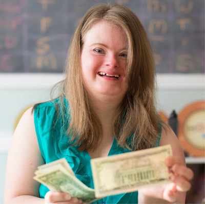 Young woman with Down syndrome smiles while holding dollar bills as she practices money management.