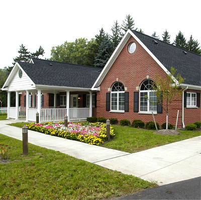 A wheelchair accessible one-level home made of red brick with a black roof and white trim, surrounded by small well-manicured hedges and a cluster of colorful flowers