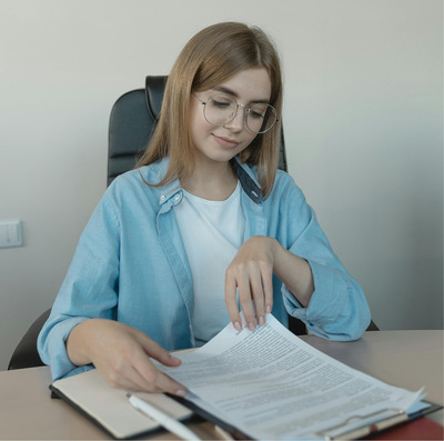 Young woman with dark blonde hair sitting in a wheelchair flips through office paperwork on a tabletop.