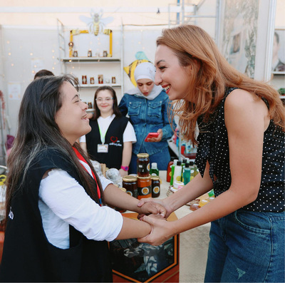 Young dark-haired woman with a disability smiles and shakes hands with another taller woman with reddish brown hair, backed by a cafe store.