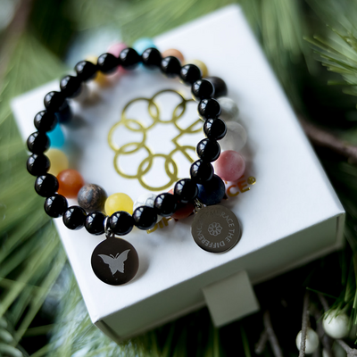 Two bracelets, one black beads the other multicolored beads on a gift box