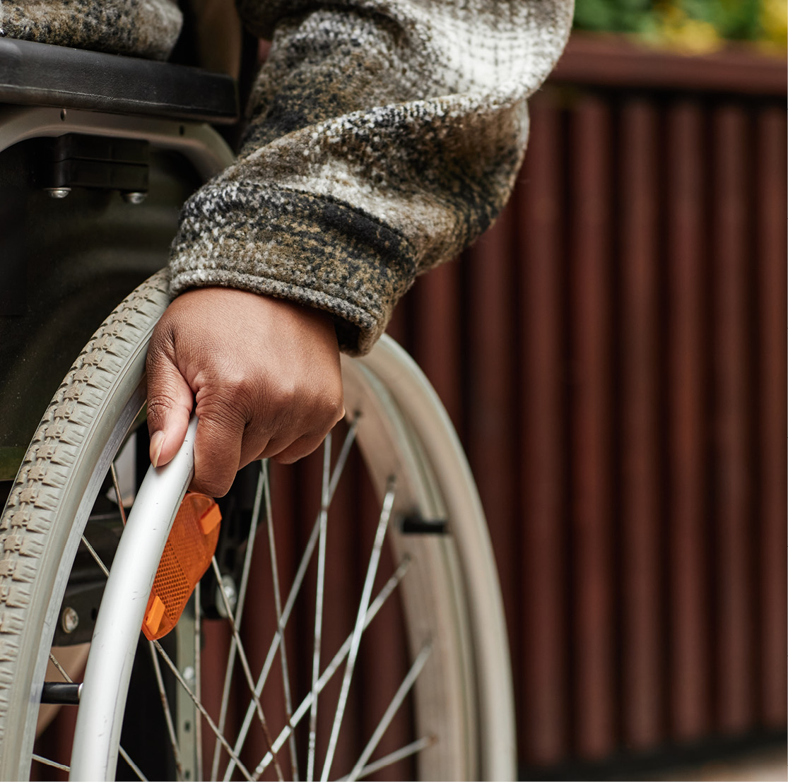 Close-up view of a wheelchair user's hand on the wheel of their chair, navigating a wooden accessibility ramp.