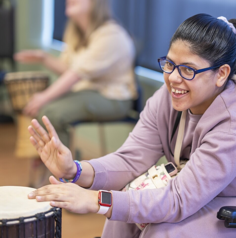 Young woman who uses a wheelchair tapping a drum in a studio