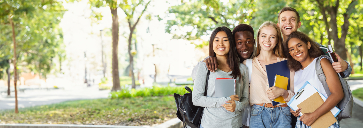 Diverse group of students holding notebooks and smiling, standing on wooded path.